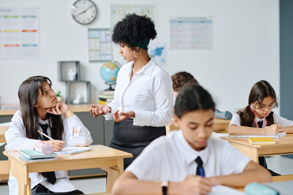 School teacher explaining something to school girl in classroom. Being away from school can mean being away from structure, regular socialisation, and sufficient adult supervision.