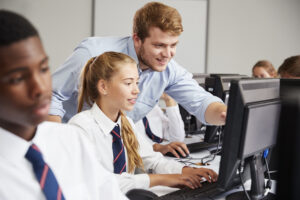 Secondary students on a computer being helped by their teacher.